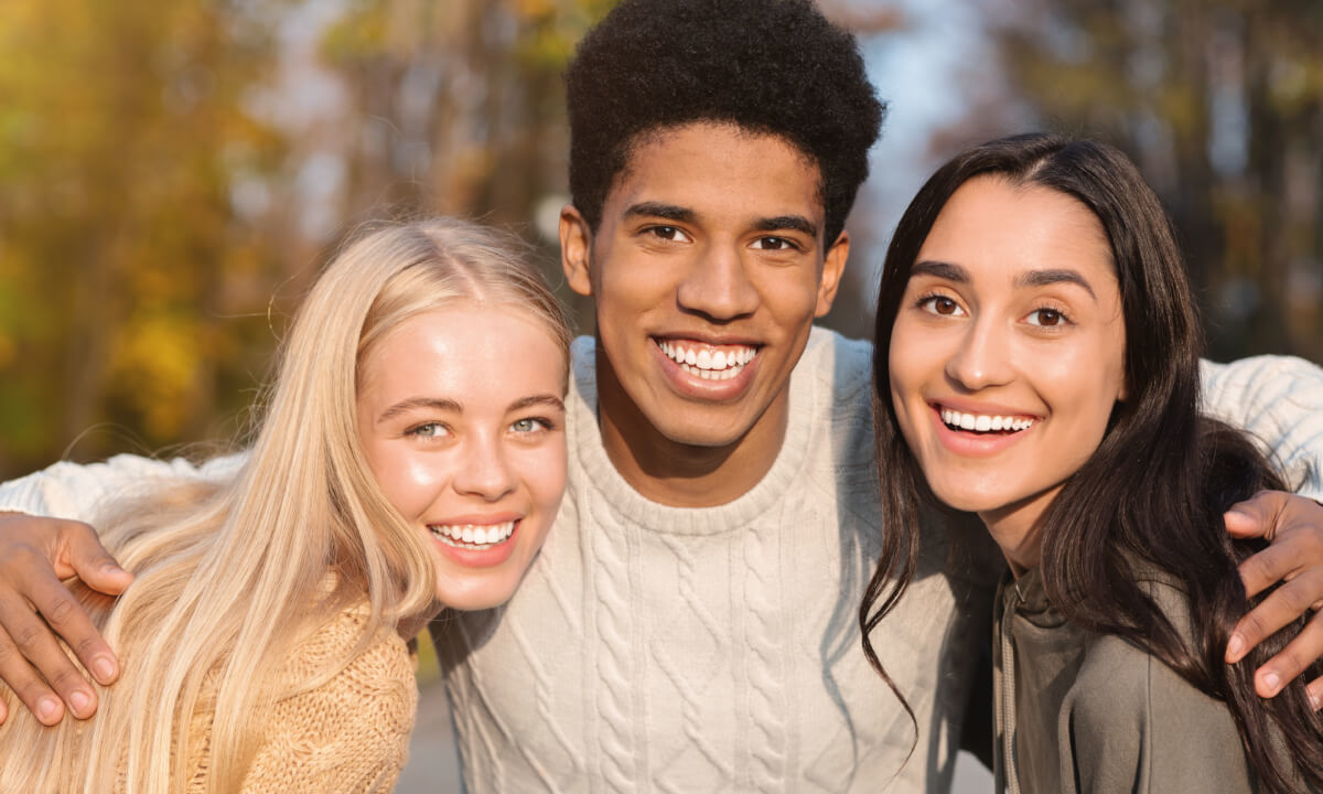 Two teenage girls and one boy hugging, smiling together