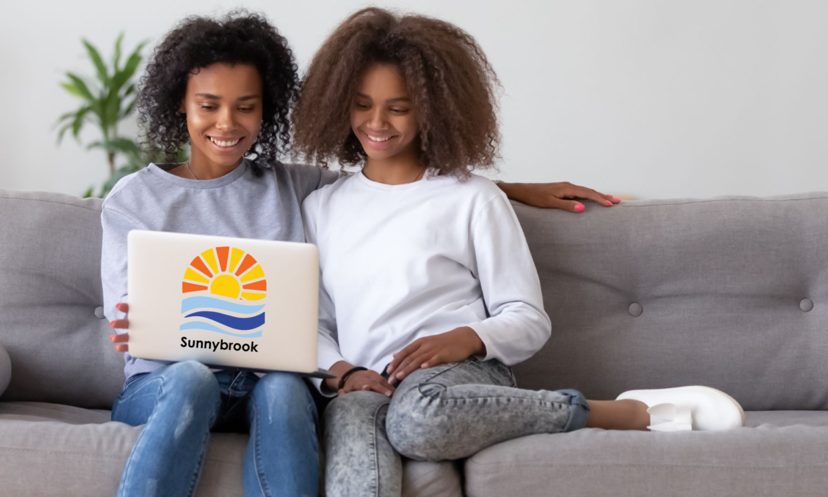 Two teenage girls smiling, sitting on a couch looking at a computer